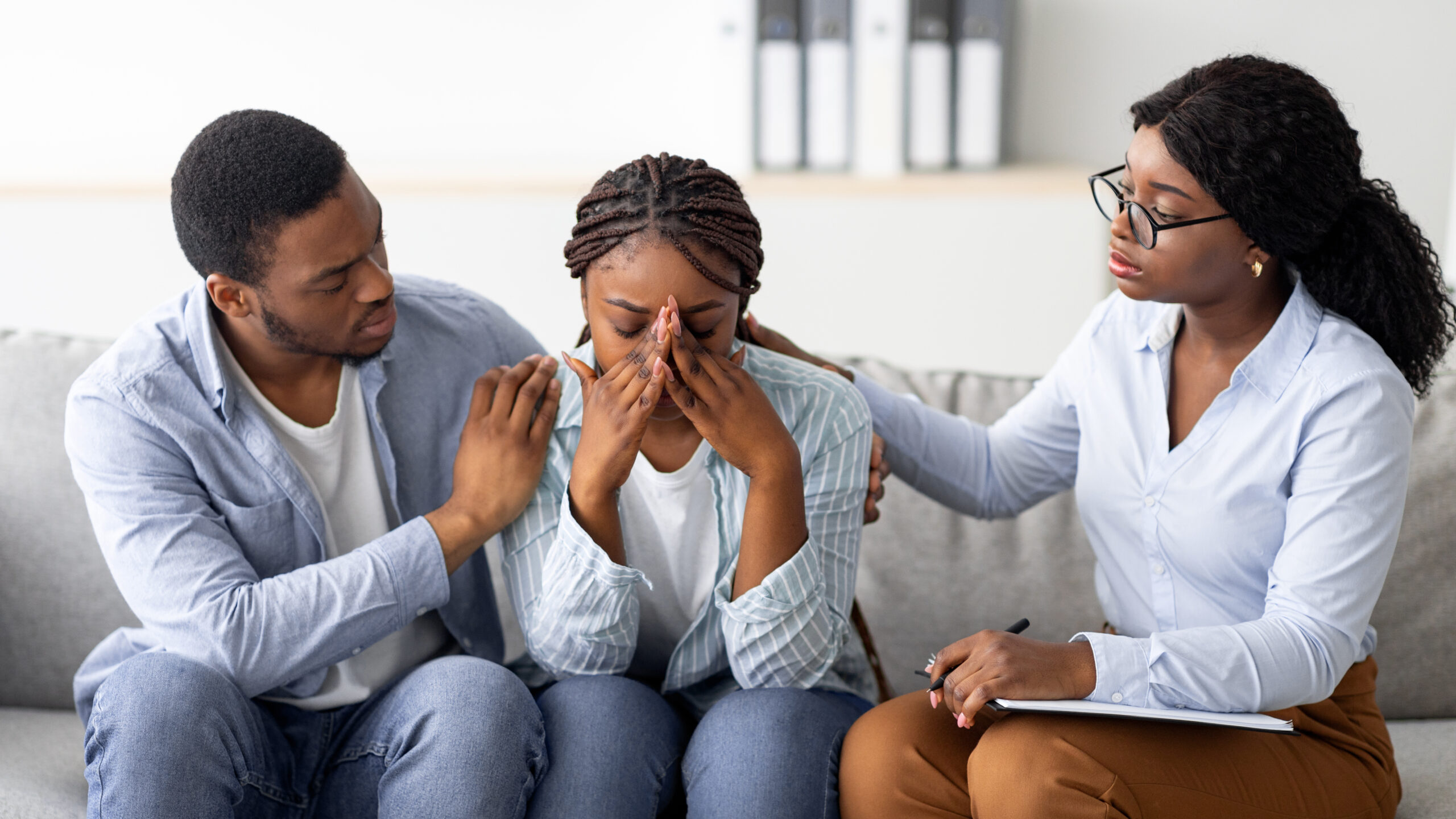 young black woman crying at therapist's office, affectionate husband supporting her with professional psychologist